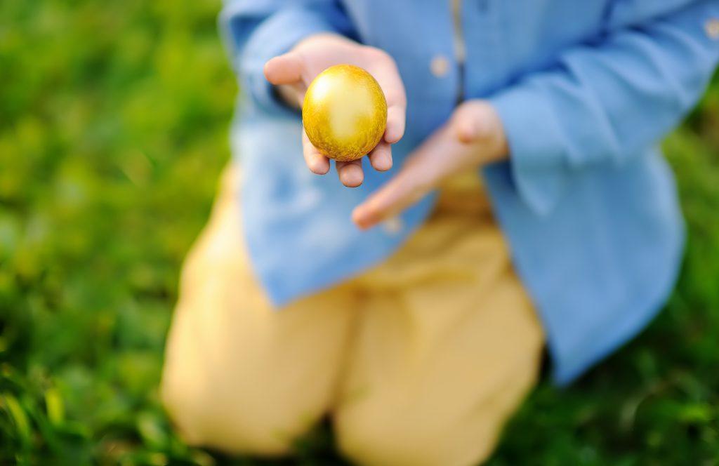 Close-up photo of little boy hunting for easter egg in spring park on Easter day. Cute little child celebrating feast outdoors